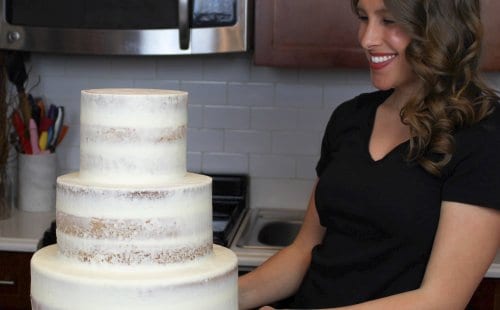 这是一张三层半裸婚礼蛋糕的照片，蛋糕上有奶油芝士糖霜