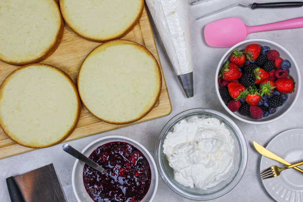 松软的白色蛋糕层、混合的浆果蛋糕馅料和奶油芝士马斯卡彭霜层的图像，并准备用于制作浆果香肠蛋糕