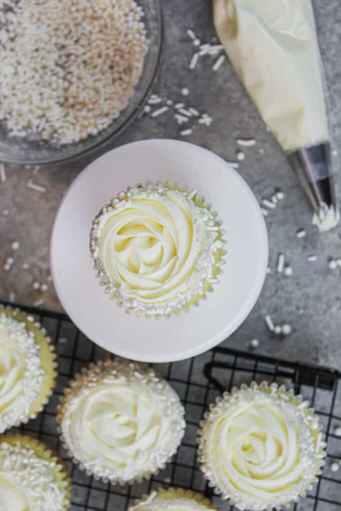 这是一个装饰着100万威尔顿糖霜头和花哨的白色混合洒的杏仁纸杯蛋糕