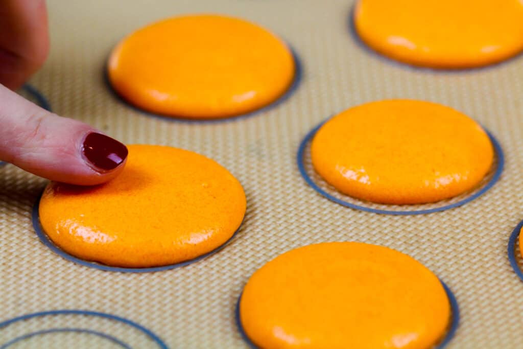 在硅垫和休息的橙色macarons的图象在被烘烤之前形成一个皮肤