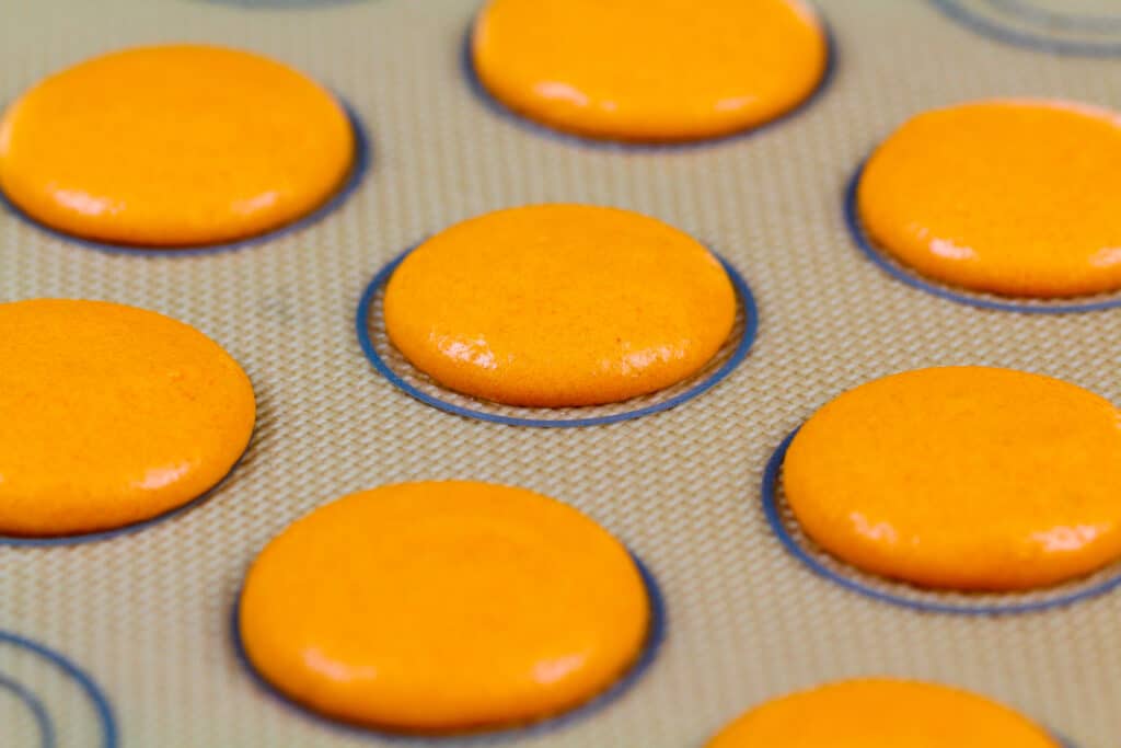 被用管道的橙色法国macaron面团的图象在硅砾垫上做南瓜macarons