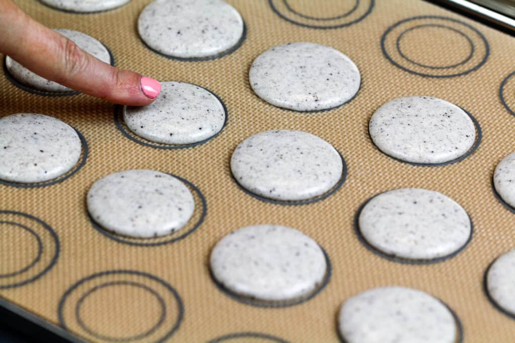 马卡龙的外壳被管道放在垫子上，在烘烤前休息形成皮