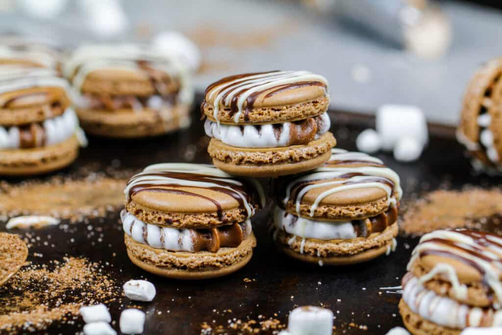 热可可马卡龙装满了热可可和棉花糖奶油，堆放在托盘里，周围是迷你棉花糖