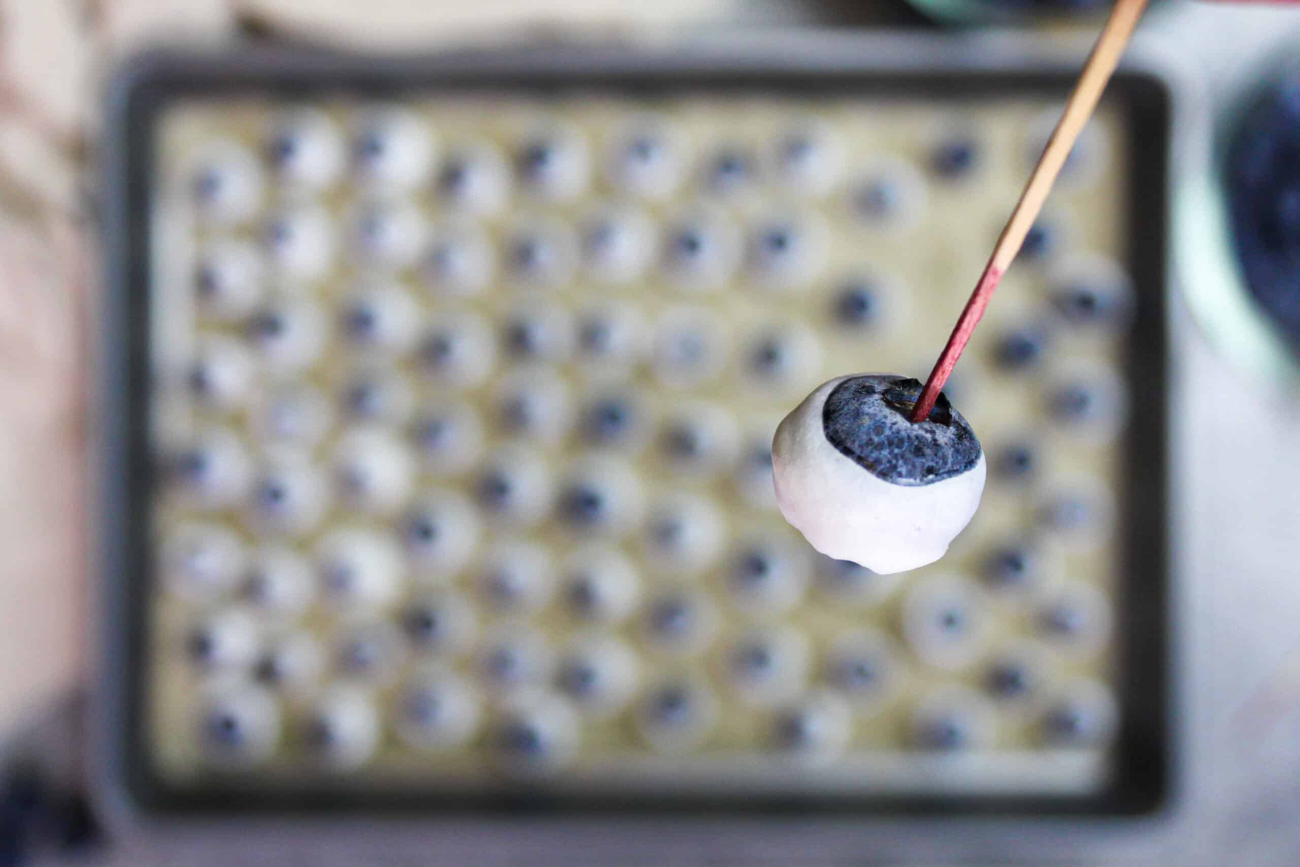 一个用牙签夹着的冻酸奶蓝莓的图片