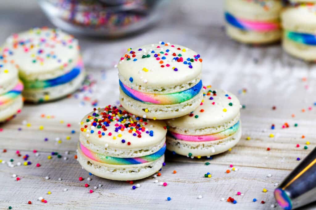 三个彩虹马卡龙堆叠在一起，炫耀他们的顶部和彩虹奶油