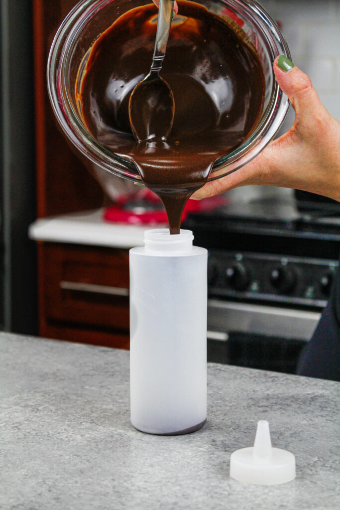 被倒入塑料喷泉瓶的巧克力ganache的图象添加滴水到蛋糕