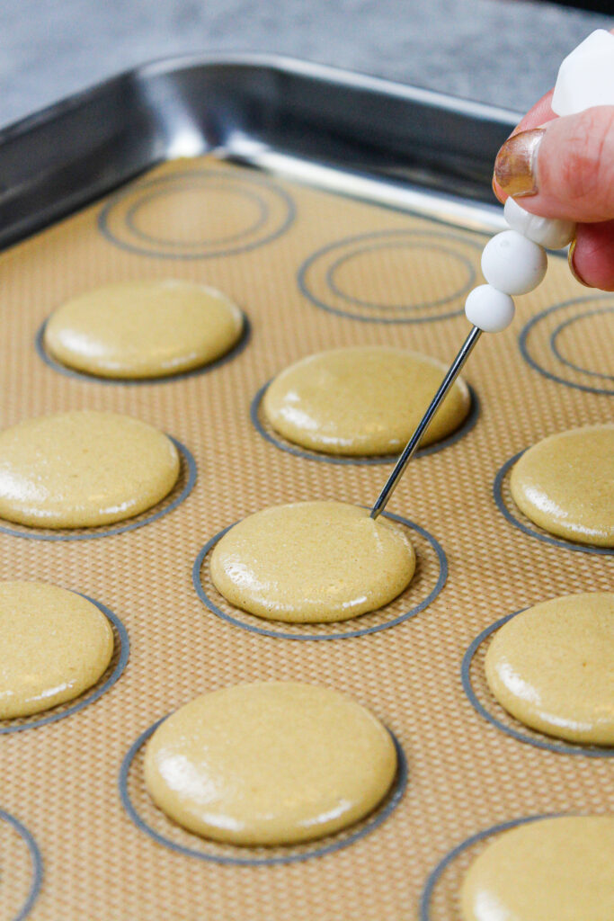 这是咖啡马卡龙的外壳被管子管着，敲击在柜台上释放出任何气泡，这些气泡正在被一个划线器戳破