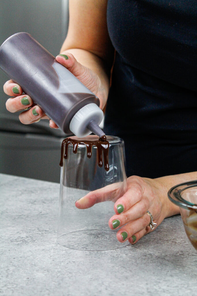 巧克力甘纳许滴在一个高玻璃杯周围，以测试其一致性和实践添加滴到蛋糕