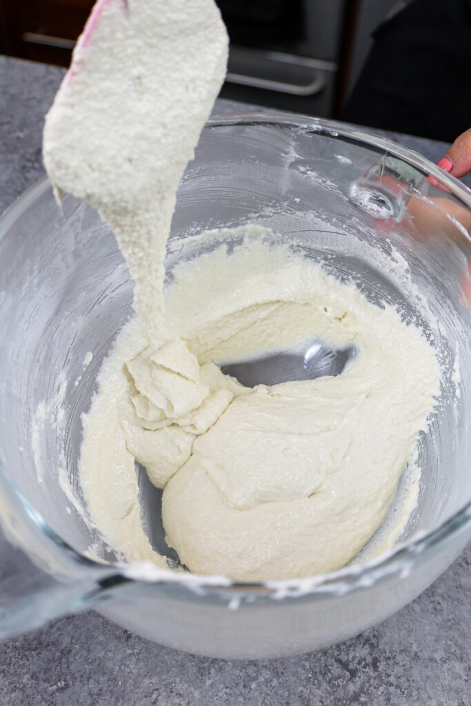 流下在厚实的丝带的橡胶刮刀的白色香草macaron面糊的图象表明它已经完全混合并且准备好被送礼