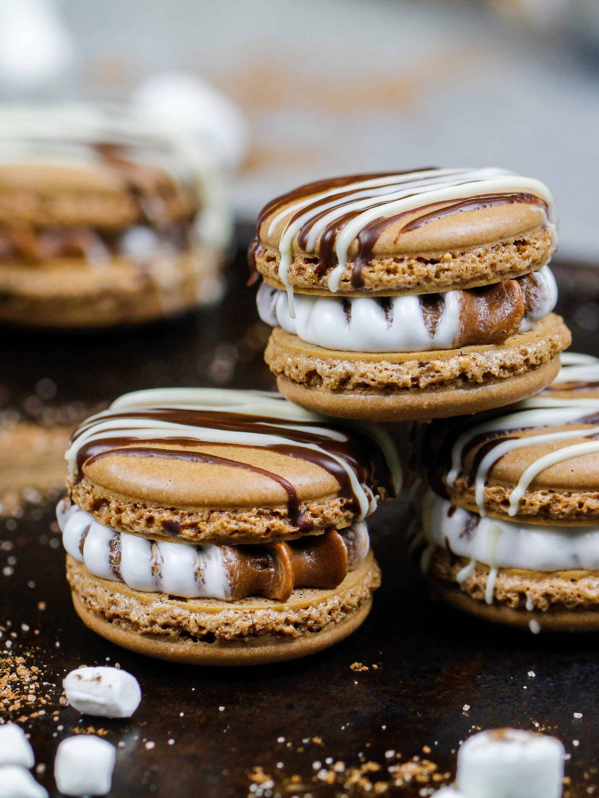 热可可马卡龙的图像，充满了热可可和棉花糖奶油奶油，它们被堆叠在一起的托盘包围着小棉花糖